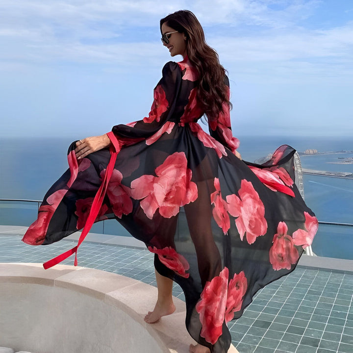 Femme portant un kimono long et fluide à motifs floraux rouges et noirs. Kimono de notre collection, idéal pour un style élégant et décontracté. Vue sur mer en arrière-plan.