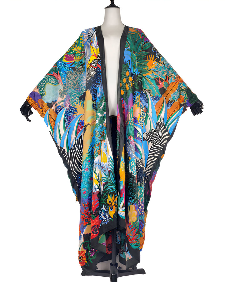 Kimono long multicolore à motifs floraux et tropicaux, bordure noire. Vêtement ample et élégant, idéal pour un look unique. Disponible dans notre boutique en ligne.