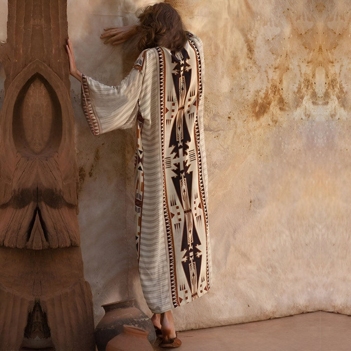 Femme portant un kimono long à motifs ethniques beiges et marrons. Kimono ample avec manches larges. Style bohème et décontracté. Vente de kimonos en ligne.