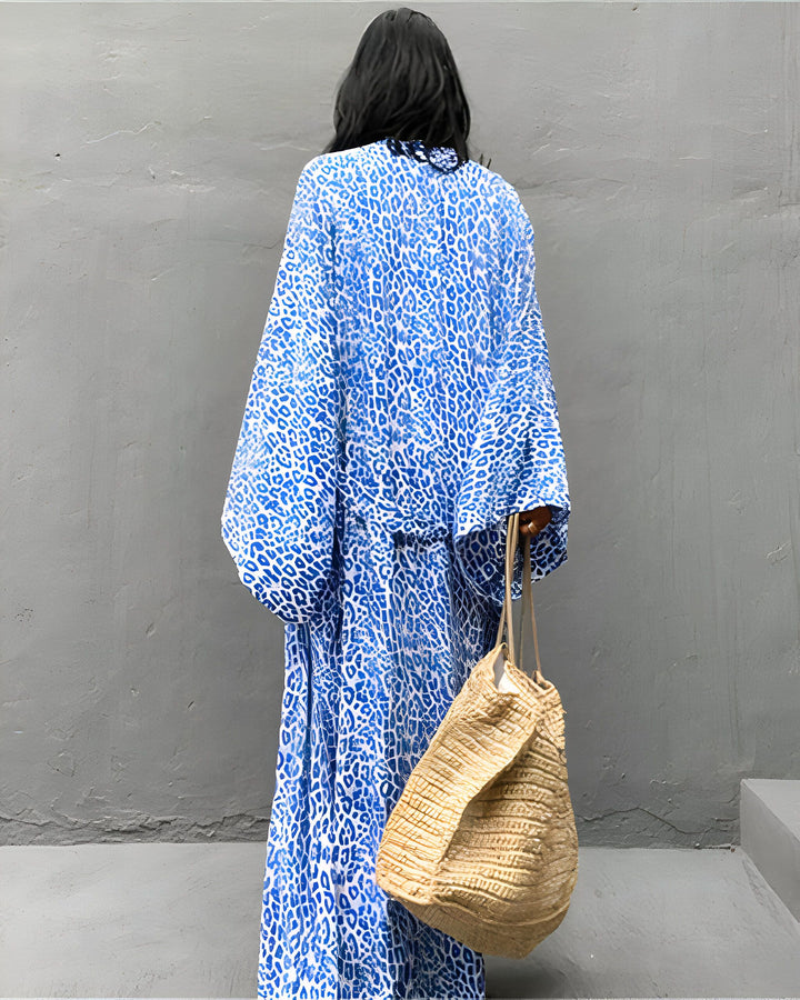Femme de dos portant un kimono long bleu à motif animalier, tenant un sac en paille. Élégance et style décontracté. Découvrez notre collection de kimonos uniques.