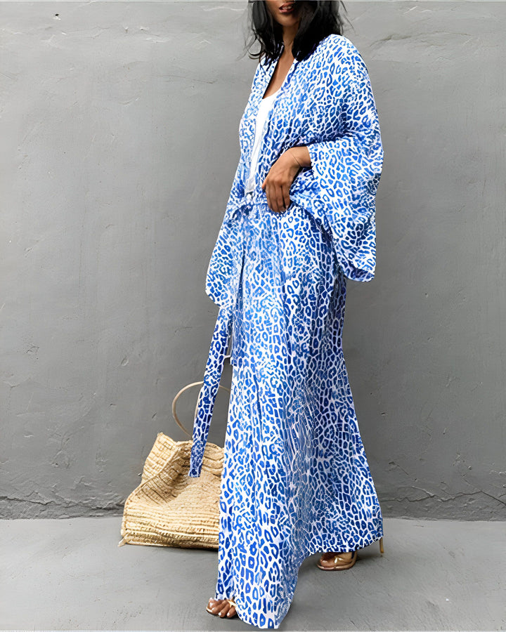 Femme portant un kimono et un pantalon assorti, motif léopard bleu et blanc. Vêtements amples et confortables. Sac en paille à côté. Mode kimono tendance.