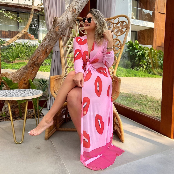 Femme souriante assise dans un fauteuil en rotin, portant un kimono rose imprimé de lèvres rouges. Mode kimono tendance. Vente de kimonos originaux. Style décontracté et élégant.