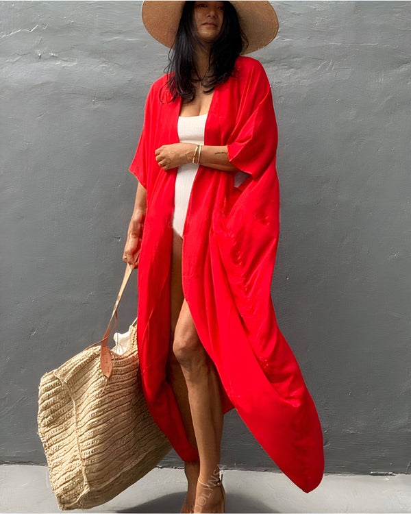 Femme portant un kimono rouge vif et un chapeau de paille, tenant un grand sac tressé. Élégance décontractée pour l'été. Découvrez notre collection de kimonos uniques.