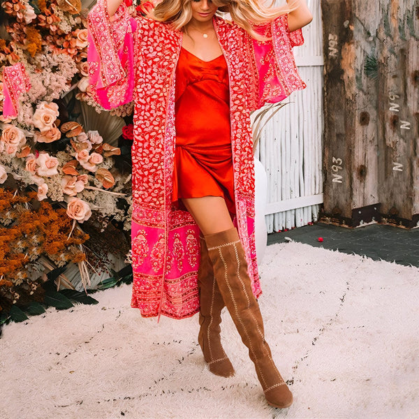 Femme portant un kimono rose à motifs fleuris avec une robe rouge, des bottes hautes marron. Vente de kimonos en ligne.