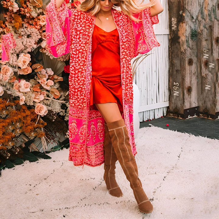 Femme portant un kimono rose à motifs fleuris avec une robe rouge, des bottes hautes marron. Vente de kimonos en ligne.