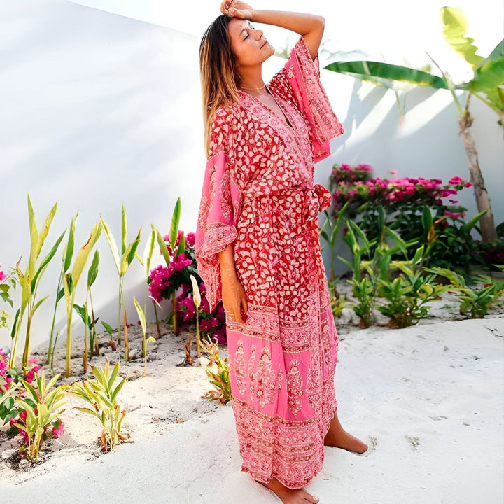 Femme portant un kimono long rose et rouge à motifs floraux. Vêtement de plage ample avec une ceinture, idéal pour l'été. Collection de kimonos pour femmes. Style bohème et décontracté.