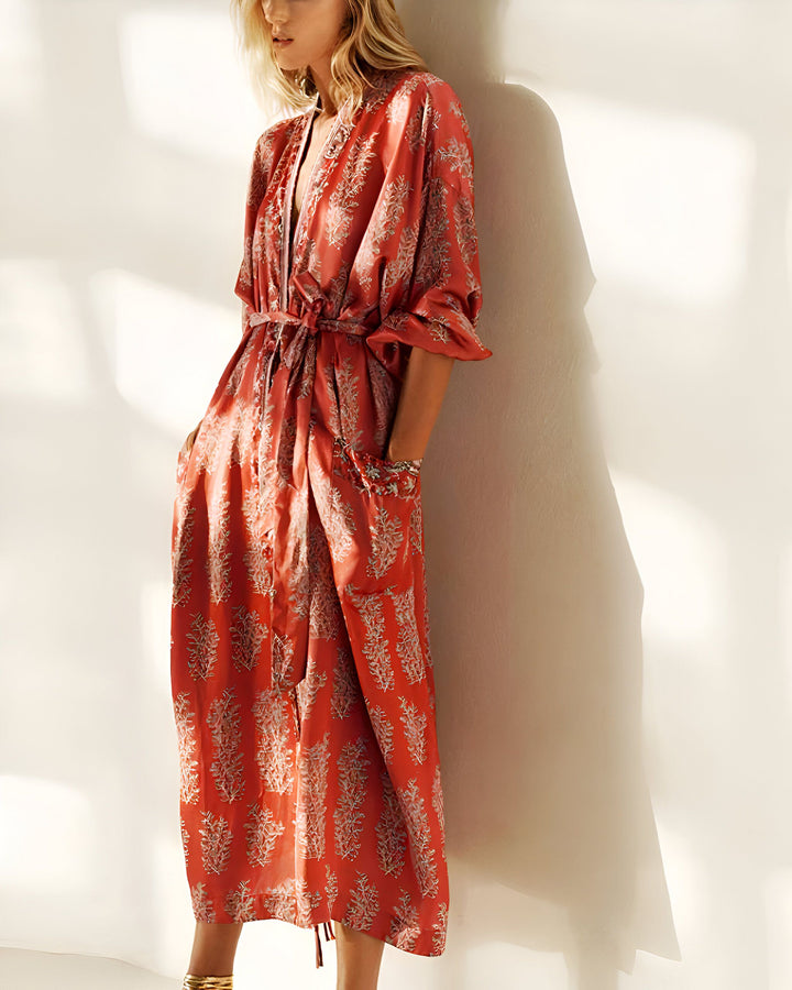 Femme portant un kimono rouge imprimé à motifs floraux. Ceinture nouée à la taille et poches. Vêtement d'intérieur élégant et confortable. Collection de kimonos disponibles en ligne.