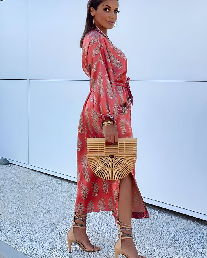 Femme portant un kimono long rose à motifs, avec ceinture, sac en bambou et talons hauts. Élégance et style kimono.