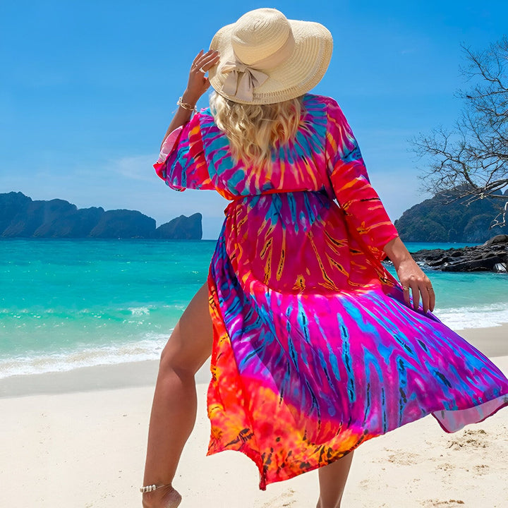 Femme portant un kimono coloré sur une plage tropicale. Kimono tie-dye rose, orange et bleu, chapeau de paille. Collection de kimonos pour femmes.