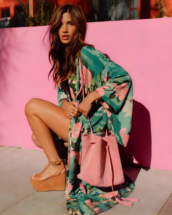 Femme accroupie portant un kimono fleuri vert et rose, sac rose assorti. Look estival et bohème. Kimonos tendance en vente.