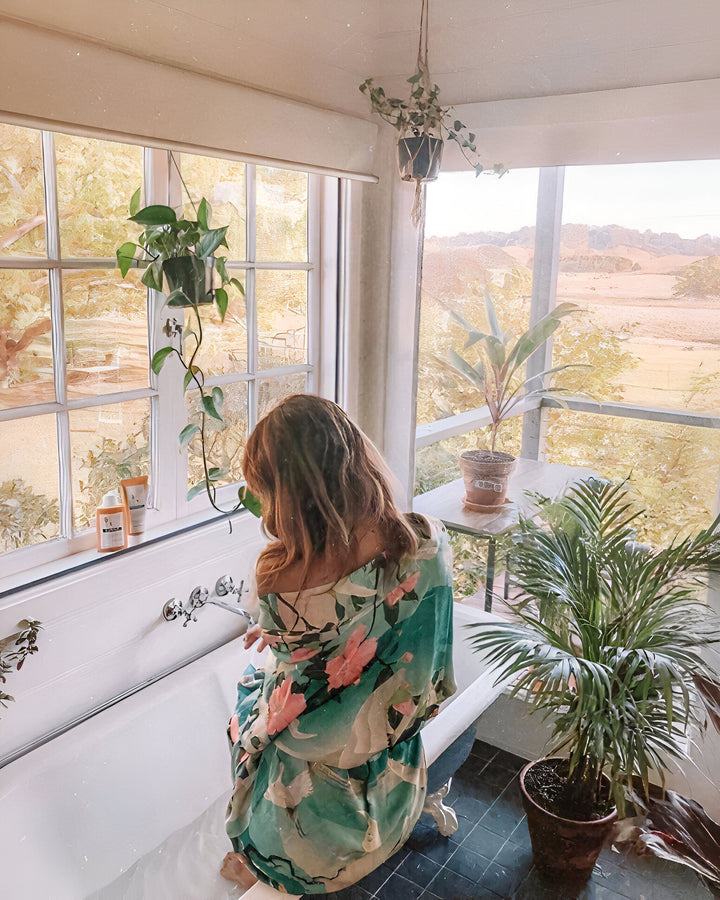 Femme de dos en kimono fleuri relaxant dans une baignoire vintage près d'une fenêtre lumineuse avec vue sur la nature. Ambiance zen et élégante. Vente de kimonos.