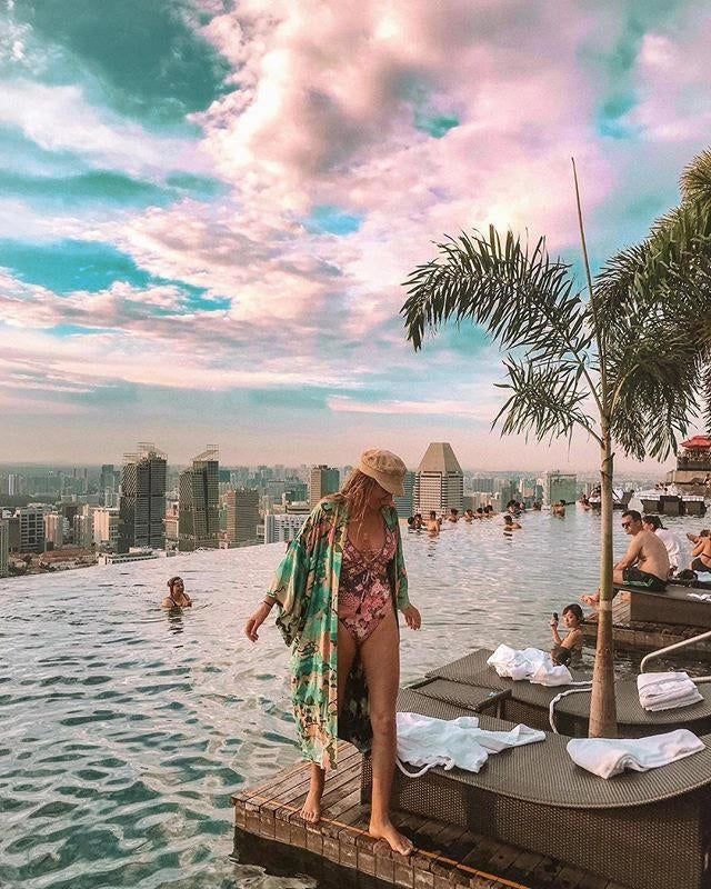 Femme en kimono coloré au bord d'une piscine à débordement avec vue sur la ville. Kimonos de plage à vendre.