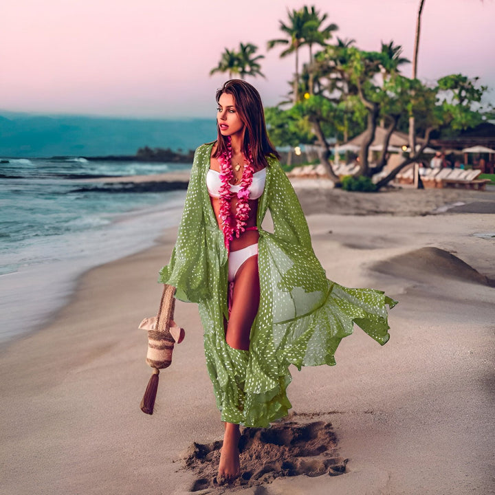 Femme en kimono vert à pois sur la plage avec bikini blanc et collier de fleurs roses. Vente de kimonos pour femmes. Mode estivale, plage tropicale avec palmiers au coucher du soleil.