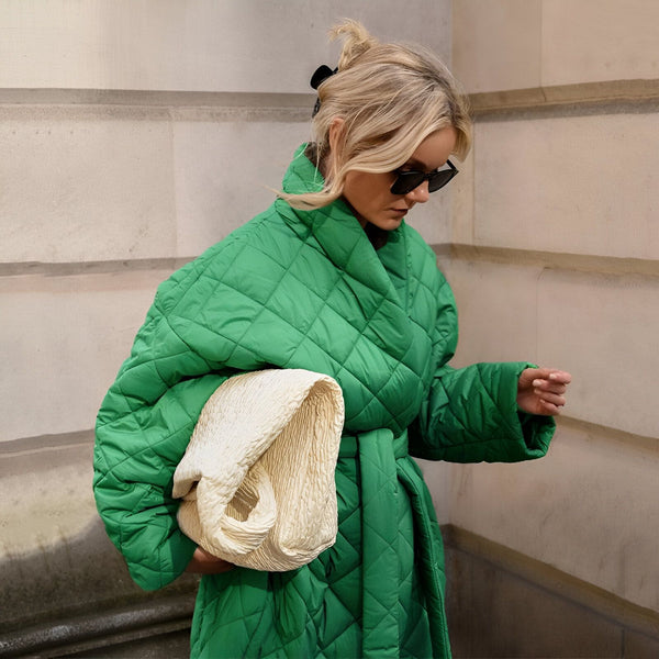 Femme blonde portant un kimono vert matelassé avec ceinture et lunettes de soleil. Elle tient un sac blanc texturé. Découvrez notre collection de kimonos tendance!