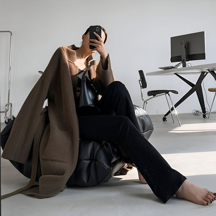 Femme assise portant un kimono marron ample, jean noir évasé et sac noir. Style décontracté et élégant, parfait pour compléter votre garde-robe. Découvrez notre collection de kimonos uniques !