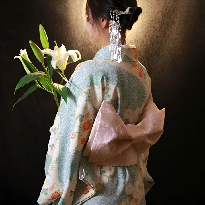Femme de dos en kimono traditionnel japonais avec des motifs floraux et marins, coiffure ornée d'accessoires argentés, tenant des lys blancs. Vêtements japonais, kimonos à vendre.