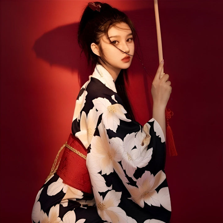 Jeune femme portant un kimono à fleurs noir et blanc, avec une ceinture rouge. Elle tient un parasol. Kimonos pour femmes disponibles à l'achat en ligne.