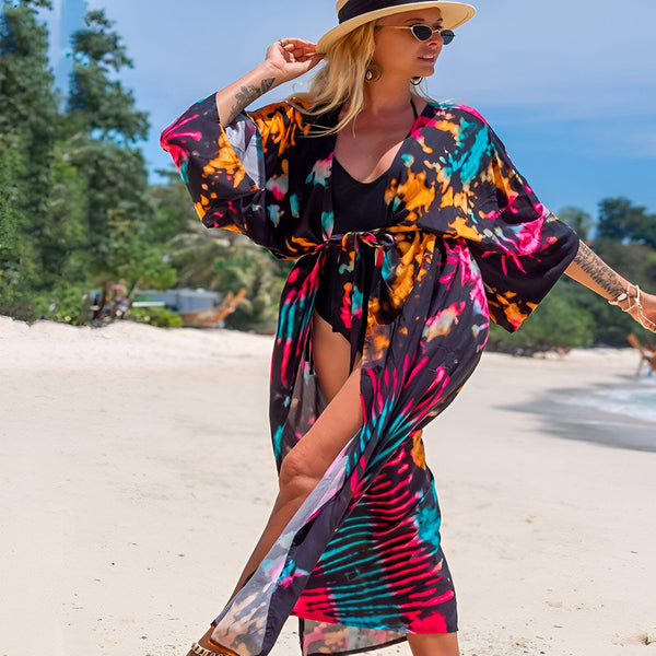 Femme blonde à la plage, portant un kimono coloré, un maillot de bain noir et un chapeau de paille. Kimonos pour femmes, vêtements de plage. Achetez des kimonos uniques en ligne.