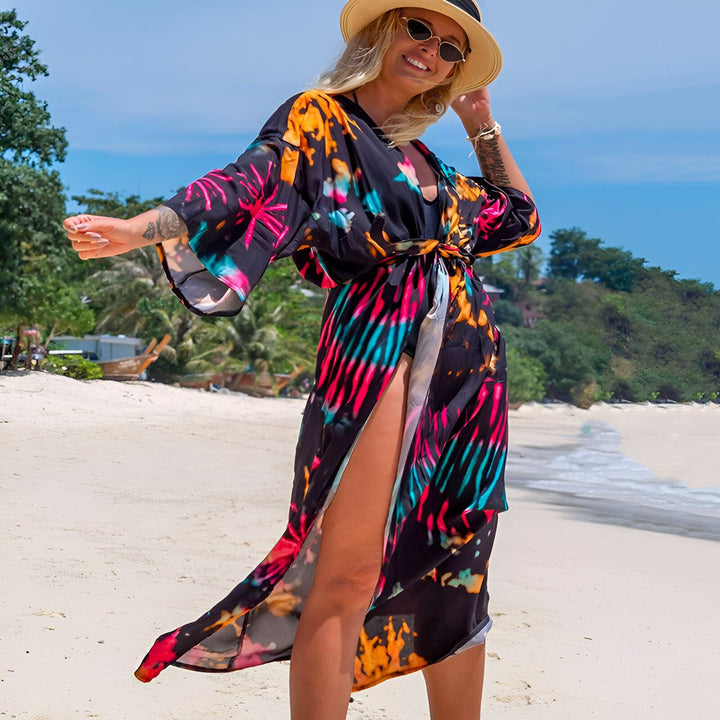 Femme souriante à la plage portant un kimono coloré, chapeau et lunettes de soleil. Kimonos pour femmes disponibles à l'achat.