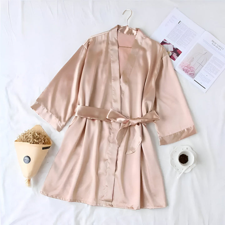 Kimono rose en satin avec ceinture, suspendu sur un cintre. Vêtement de détente élégant. Nos kimonos sont parfaits pour se relaxer avec style.