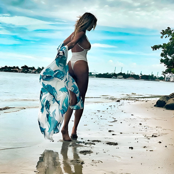 Femme en maillot de bain blanc sur la plage, portant un kimono bleu et blanc à motifs floraux. Vente de kimonos, mode plage estivale.