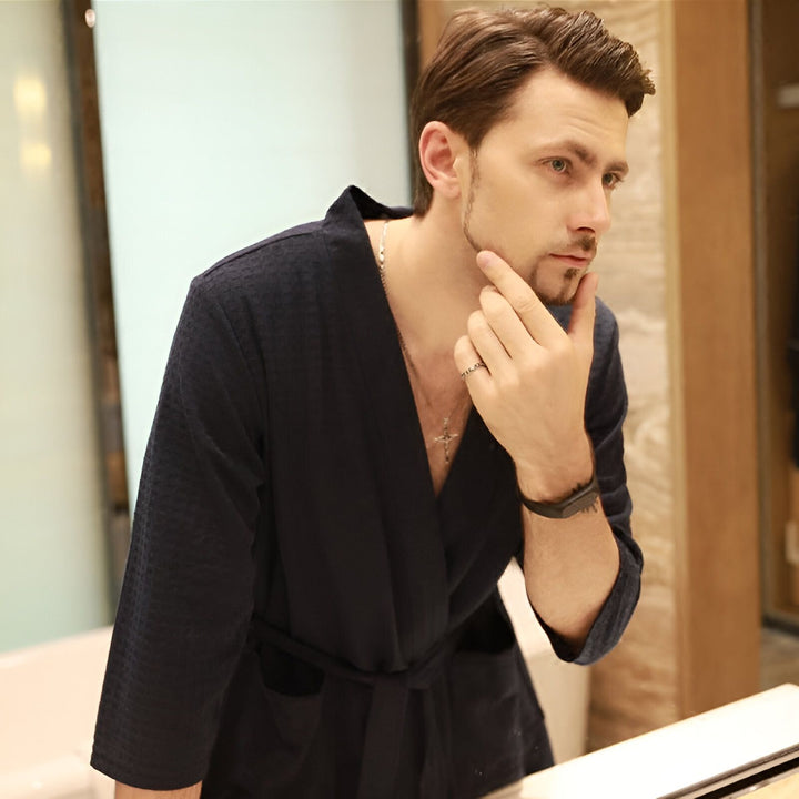 Homme portant un kimono bleu marine, se regardant dans le miroir. Peignoir kimono pour hommes disponible à l'achat.