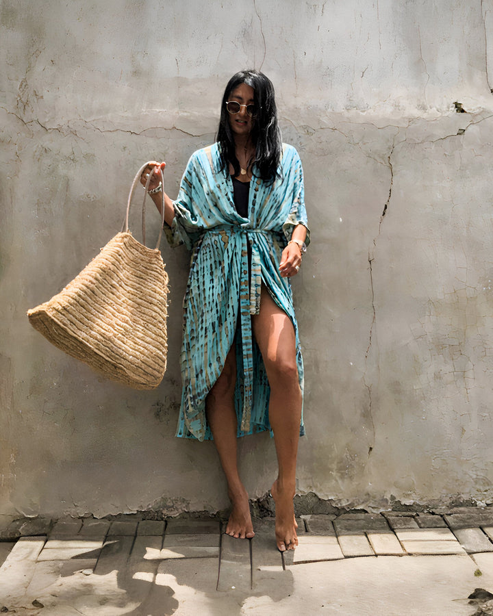 Femme portant un kimono bleu tie-dye avec une ceinture, tenant un grand sac de paille. Mode kimono pour femmes.