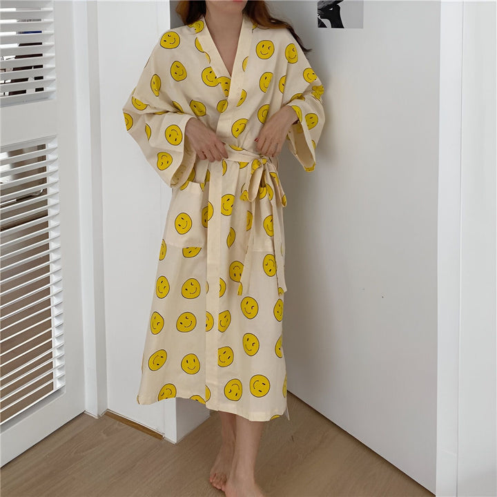 Kimono long beige à motifs de smileys jaunes, avec ceinture assortie. Vêtement d'intérieur confortable et stylé. Idéal pour se détendre avec une touche d'originalité. Kimono disponible à l'achat.