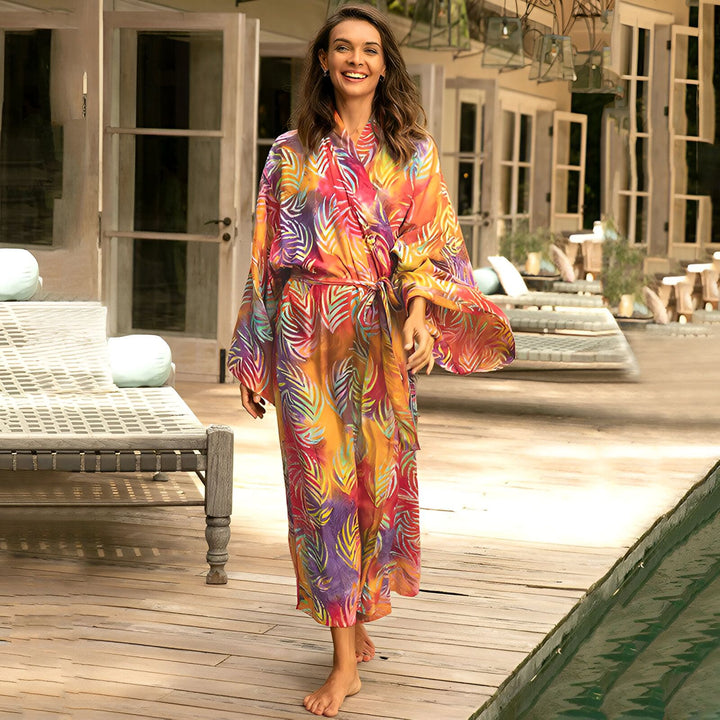 Femme souriante portant un kimono coloré à motifs de feuilles. Kimono de plage idéal pour l'été. Découvrez notre collection de kimonos en ligne.