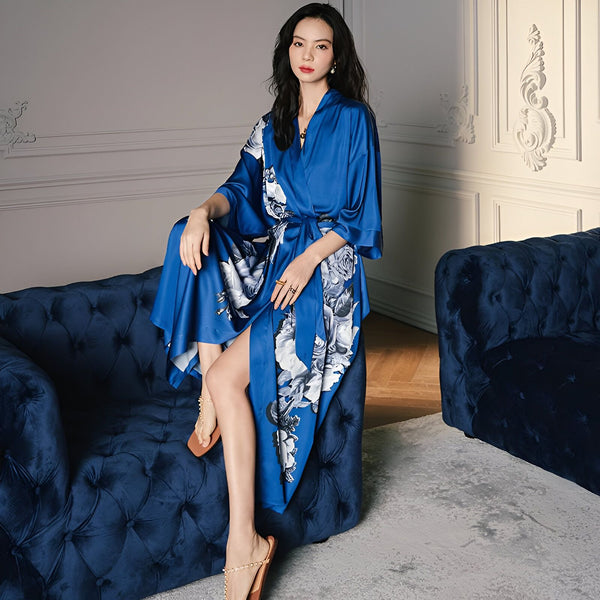 Femme élégante en kimono bleu avec motifs floraux, assise sur un canapé assorti. Idéal pour se détendre avec style. Collection de kimonos de luxe.