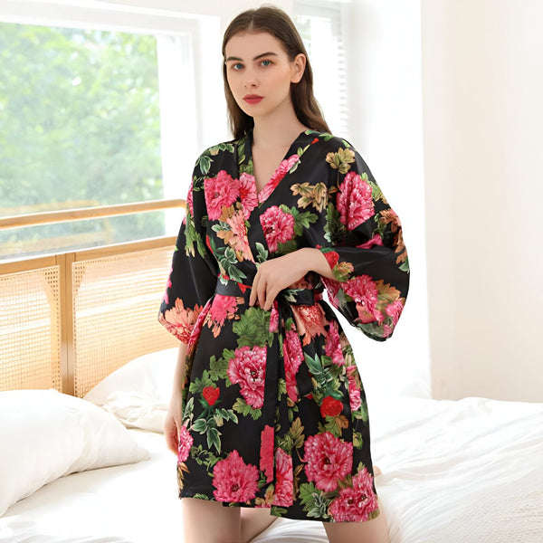 Femme portant un kimono noir à motifs floraux roses. Peignoir style japonais avec ceinture. Vêtements de détente élégants. Kimonos pour femmes à la mode.