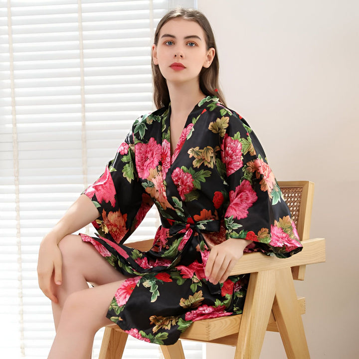 Femme portant un kimono noir à fleurs roses et vertes. Peignoir de style japonais en soie ou satin, disponible à l'achat. Vêtements d'intérieur confortables et élégants.