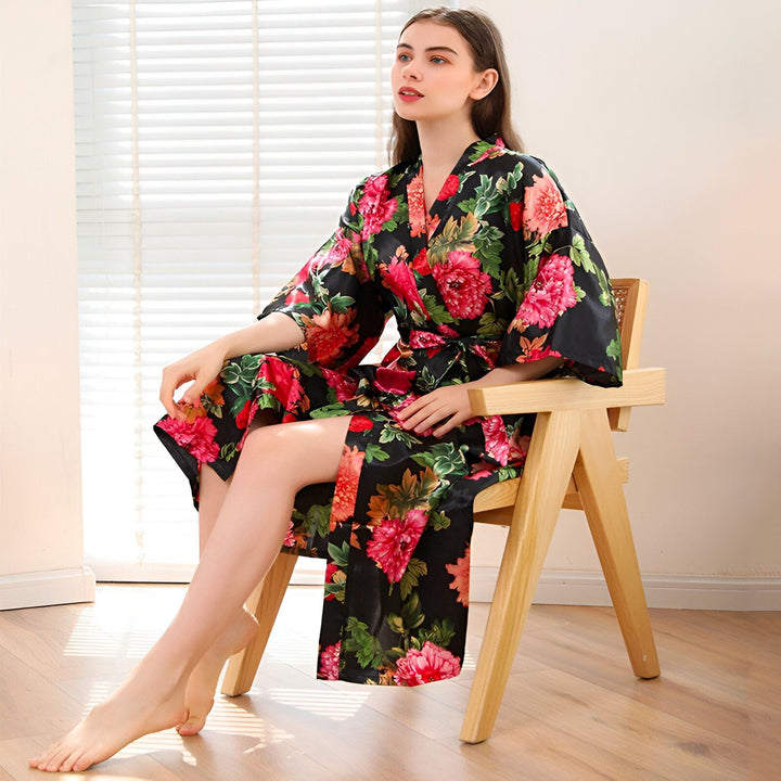 Femme assise sur une chaise, portant un kimono noir à motifs floraux roses et verts. Vente de kimonos en ligne.