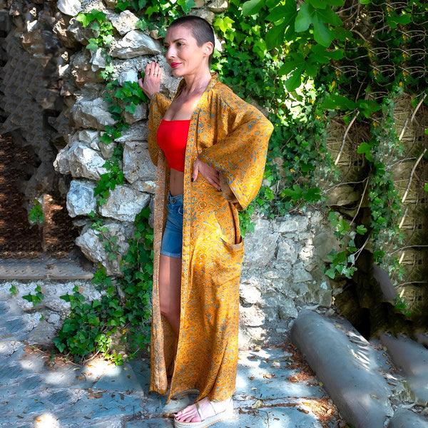 Femme portant un kimono long jaune à motifs devant un mur en pierre et de la verdure. Vêtements kimono à la mode.