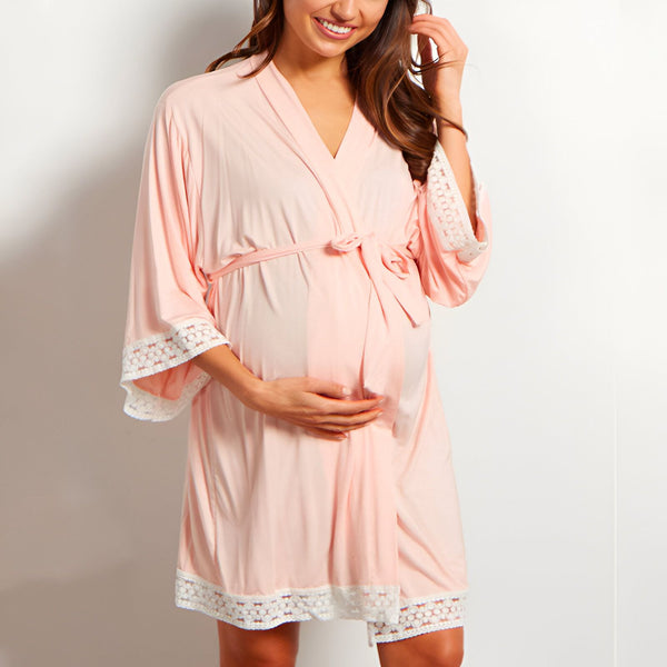 Femme enceinte souriante portant un kimono rose avec bordure en dentelle blanche, vente de kimonos maternité.