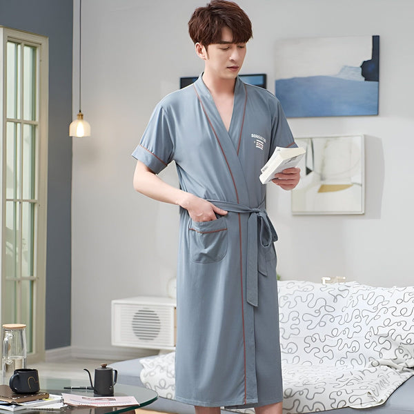 Homme portant un kimono bleu clair avec ceinture et bordure rouge, idéal pour se détendre à la maison. Vêtements de détente confortables en vente.