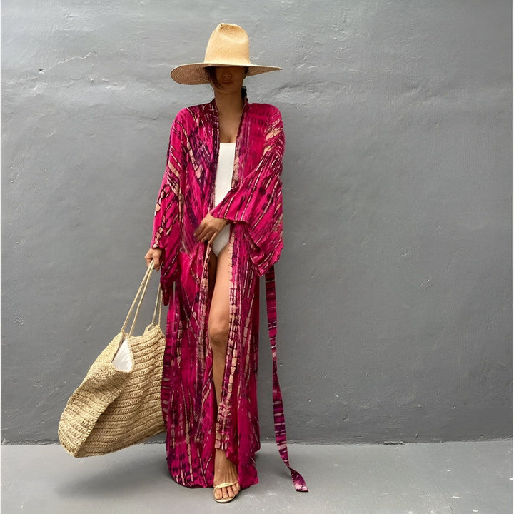 Femme portant un kimono rose tie-dye long, un chapeau de paille et un sac de plage. Vêtements de plage et tenues d'été. Découvrez notre collection de kimonos.