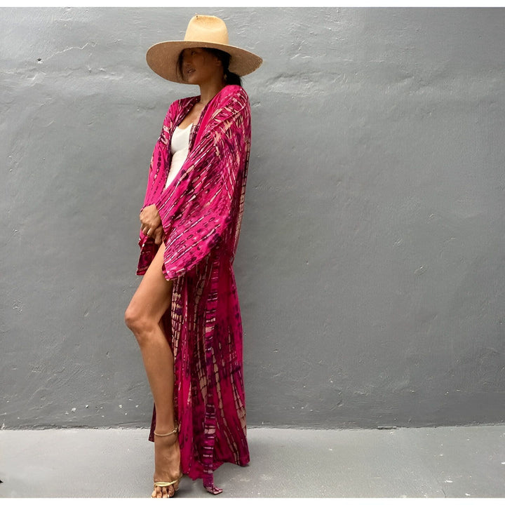 Femme portant un kimono long rose imprimé, chapeau de paille et talons dorés. Élégant et confortable, parfait pour la plage ou une soirée décontractée. Découvrez notre collection de kimonos uniques.