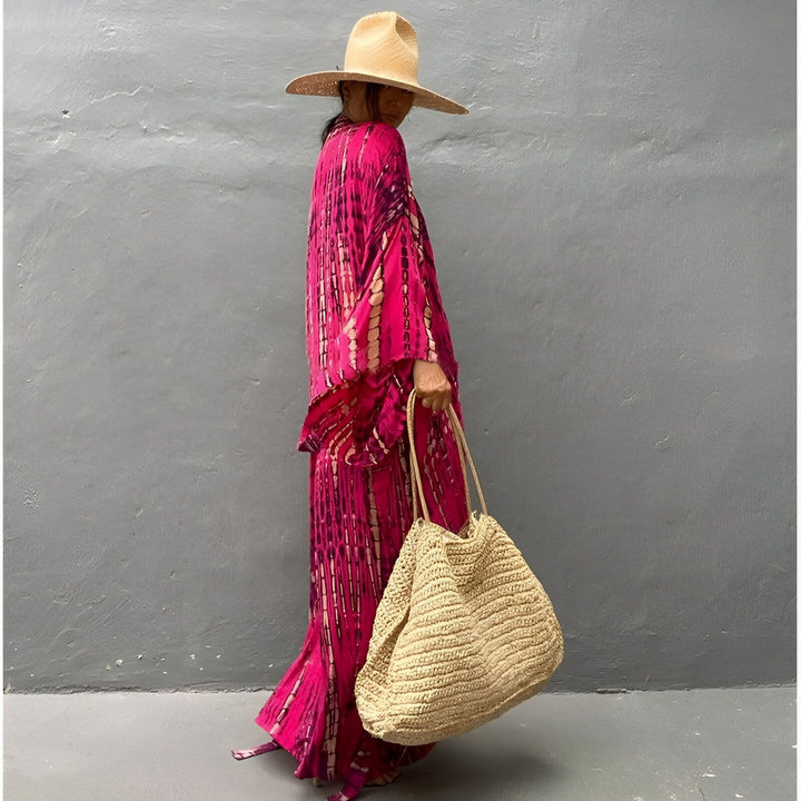 Femme portant un kimono rose tie-dye et un chapeau de paille, tenant un sac en paille. Kimonos de notre collection.