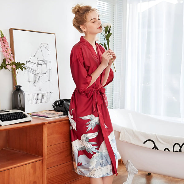 Femme portant un kimono rouge imprimé grues, avec une fleur blanche à la main, dans une salle de bain lumineuse. Idéal pour la détente et le style. Kimonos en vente.