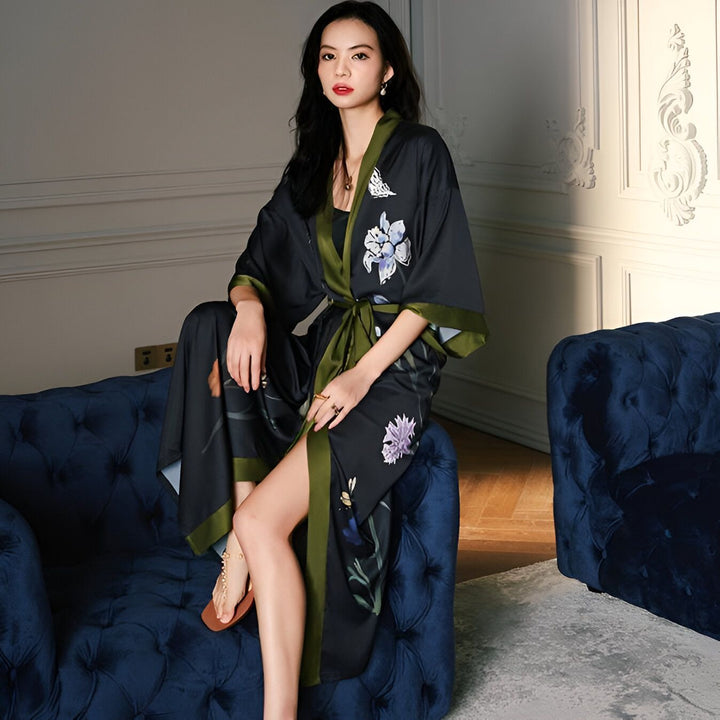 Femme assise portant un kimono noir à motifs floraux avec bordure verte. Vêtements de détente élégants. Kimonos de haute qualité disponibles à l'achat en ligne.