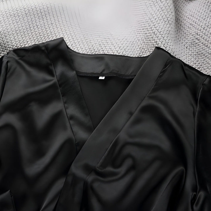 Détail d'un kimono noir en satin sur un plaid gris. Vêtement de détente élégant et confortable. Découvrez notre collection de kimonos en ligne.