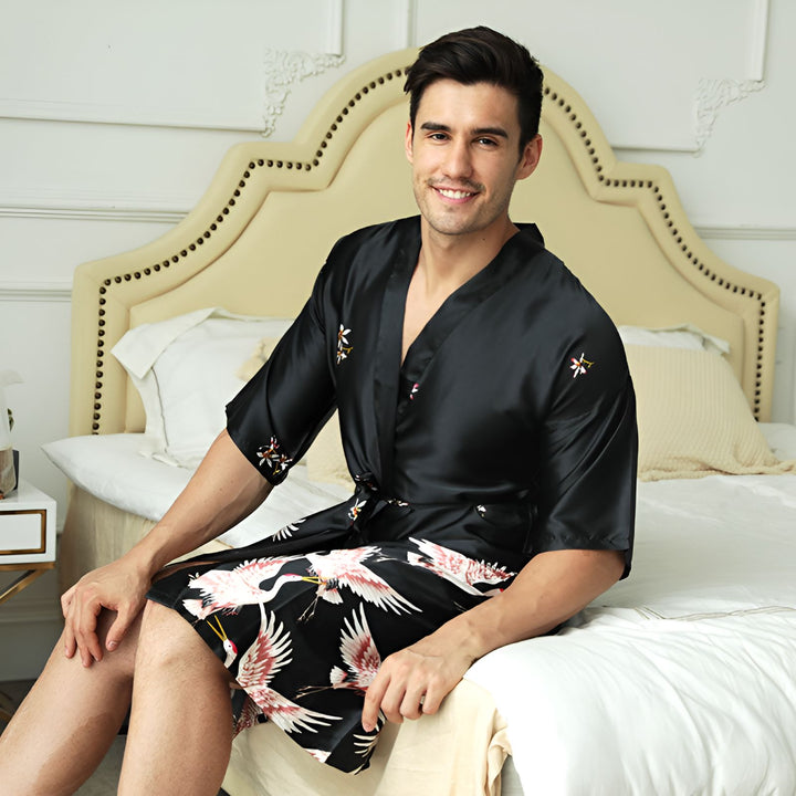 Homme souriant portant un kimono noir à motifs de grues et de fleurs. Vente de kimonos pour hommes en ligne. Élégance et confort à la maison.