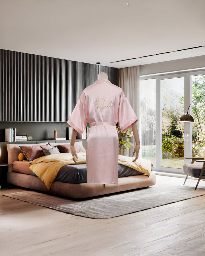 Kimono rose clair en satin sur mannequin, broderie dorée "Maid of Honor" au dos. Idéal pour un mariage élégant. Découvrez notre collection de kimonos.