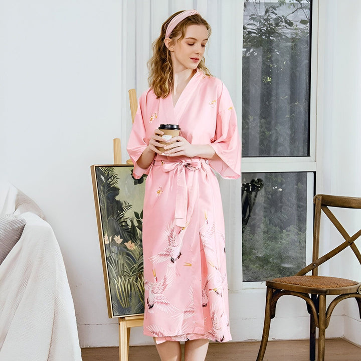 Femme portant un kimono rose à motifs de grues, tenant un café. Vente de kimonos pour femmes.