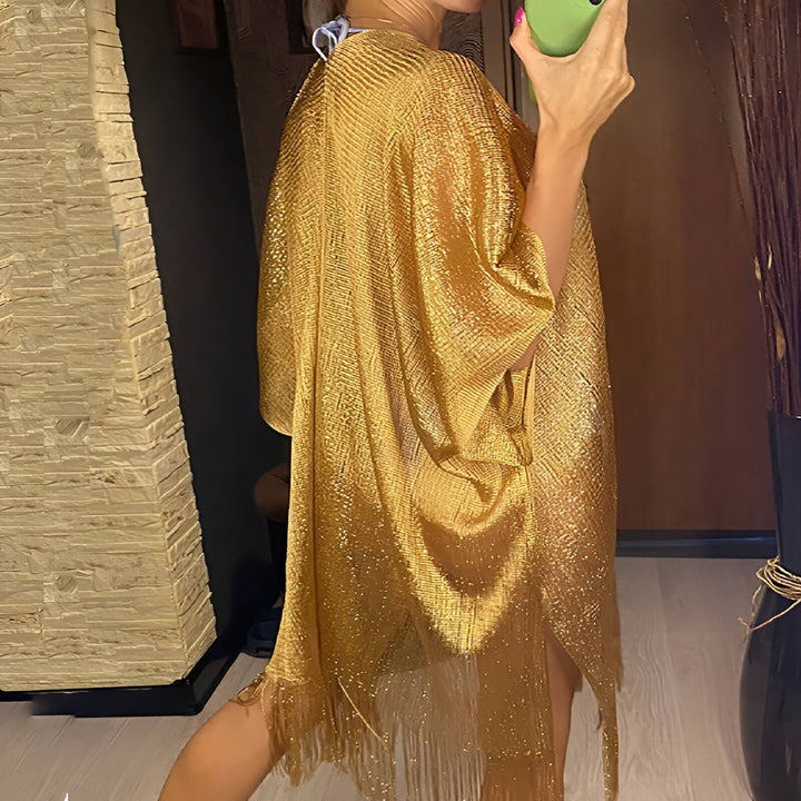 Femme portant un kimono doré scintillant avec des franges. Vêtement de mode luxueux, idéal pour compléter une tenue élégante. Découvrez notre collection de kimonos uniques.