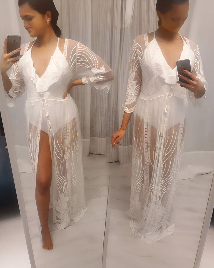 Femme devant un miroir, portant un kimono blanc transparent avec des broderies délicates. Vêtement de plage ou tenue d'intérieur élégante. Notre collection de kimonos de luxe.