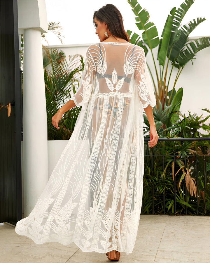 Femme portant un kimono long blanc en dentelle, dos tourné, devant une végétation luxuriante. Kimono d'été, vêtement de plage léger et élégant. Boutique en ligne de kimonos pour femmes.
