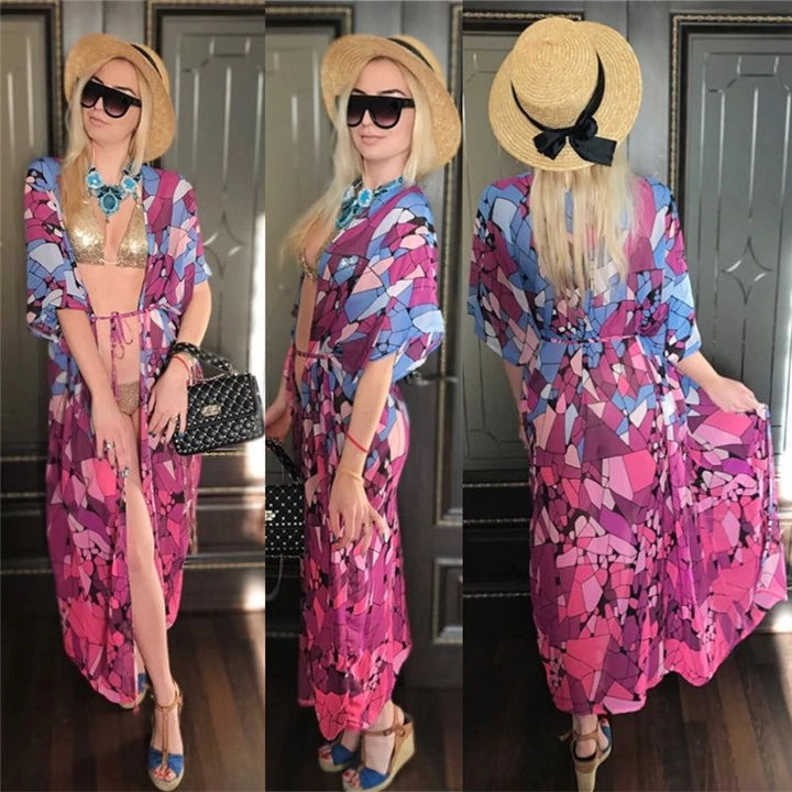 Kimono long imprimé géométrique rose et bleu porté par une femme blonde avec chapeau et lunettes de soleil. Collection de kimonos élégants pour femmes.