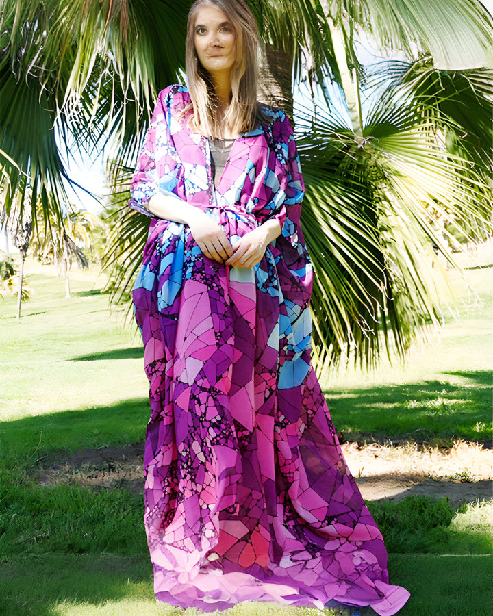 Femme portant un long kimono violet et bleu à motifs géométriques devant un palmier. Kimonos pour femmes, vêtements de plage élégants.